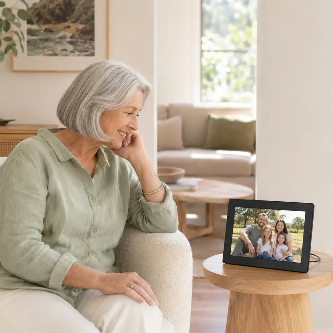 Older Australian woman viewing a black Lifeframe digital photo frame with a family photo in a bright living room.