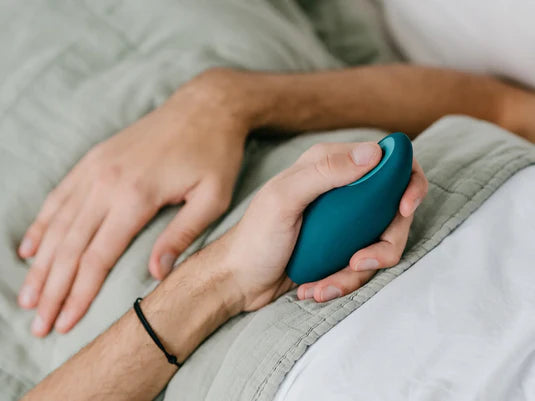 Person holding a teal Moonbird breathing device in bed to support relaxation and sleep.
